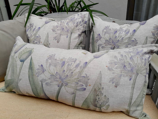 A set of cushion covers with a large print of agapanthus flowers in shades of purple, white, and green, displayed on a sofa.